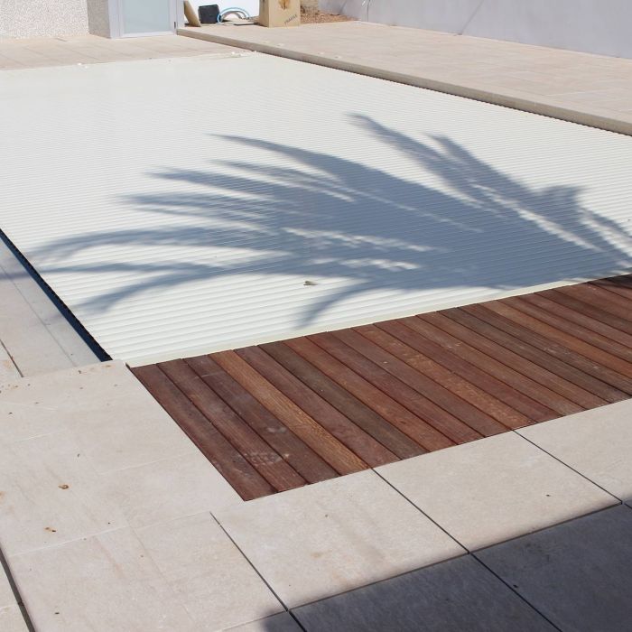 Piscina desbordante con instalación de persiana sumergida y solado de playa en gres.