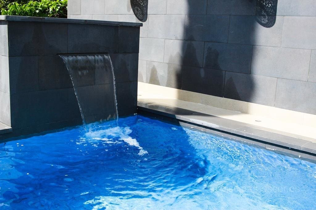 Piscina con porcelánico azul y cascada relax y decorativa