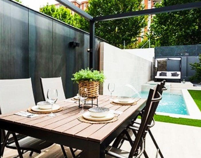 Piscina de diseño en jardín Piscina pequeña de obra con spa interior en pequeño jardín con porche y mesa preparada para comer