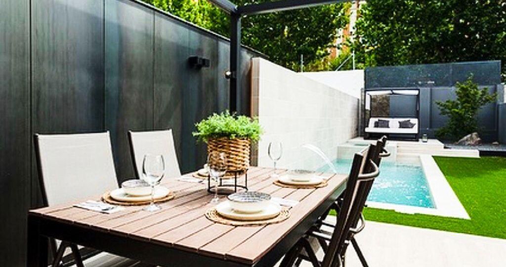Piscina pequeña de obra con spa interior en pequeño jardín con porche y mesa preparada para comer