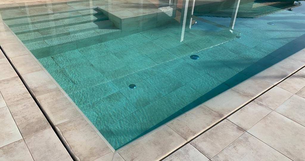 Color del agua turquesa con el porcelánico del interior de piscina igual al solado, desborde de la piscina por ranura invisible