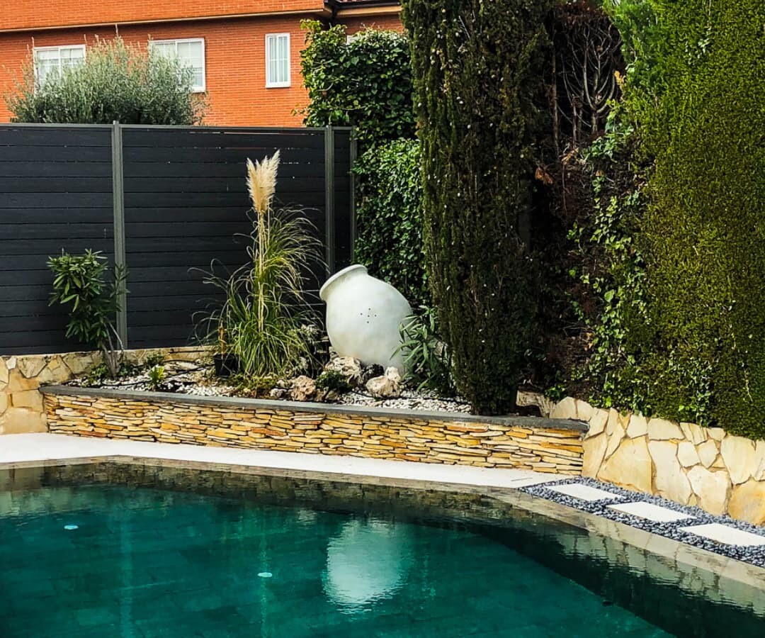 Piscina con porcelánico interior negro que contrasta con el verde del jadrín